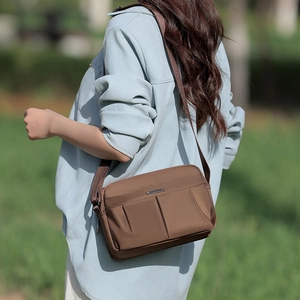 Close-up of brown canvas crossbody bag featuring front pleat pockets and metal logo detail