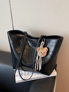 Black crocodile texture large tote bag with plush bear charm on a design book