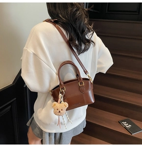 Brown leather crossbody bucket bag with plush bear charm worn by model on stairs