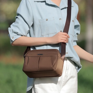 Detail of a brown nylon crossbody bag featuring a metal logo plate and wide fabric strap