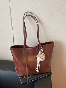 Brown crocodile pattern large tote bag with plush bear charm on black sofa