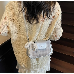 Detail of silver crossbody bag with lace bow, pearls, and heart pendant on a shoulder strap