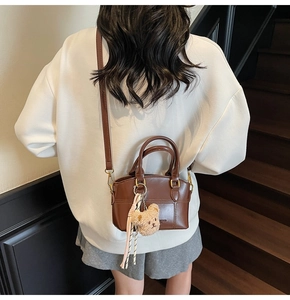 Brown PU leather bucket bag with teddy bear charm shown worn as a crossbody bag