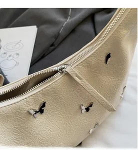 Détail d'un sac à bandoulière papillon crème avec breloques argentées et texture cuir plissé