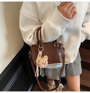 Close-up of brown leather bucket bag with gold hardware and plush bear charm detail