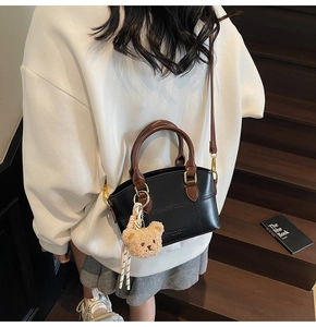 Detail of black leather crossbody bag with brown handles and a cute teddy bear charm