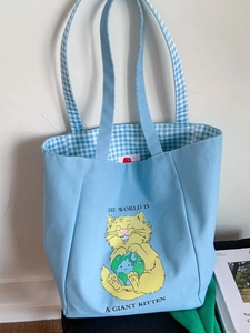 Light blue canvas tote bag with yellow cat illustration and the world is a kitten slogan