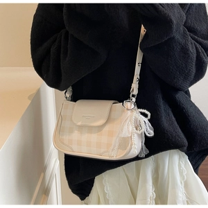 Detail of cream-colored plaid shoulder bag with pearl lace charm and magnetic flap cover