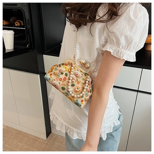 Detailed view of beige embroidered shell bag with crochet bear and pearl strap accessories