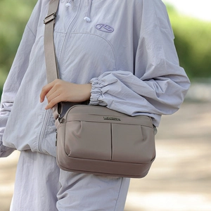 Detail of light brown crossbody bag featuring pleated design and metal logo on strap