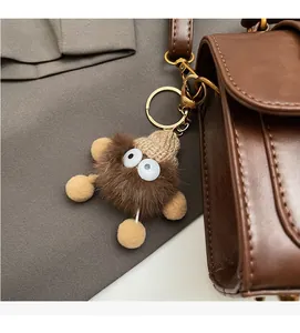 Detail of furry monster keychain with knit hat on a dark brown leather handbag