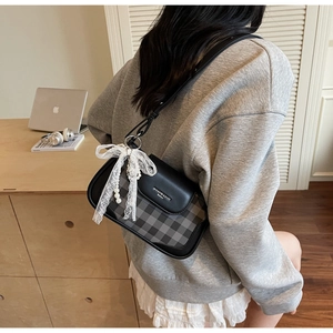 Detail of underarm bag featuring patchwork leather, plaid fabric, and lace pearl bow charm