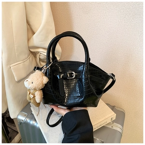 Close-up of black crocodile pattern bucket bag with a cute bear charm and buckle detail
