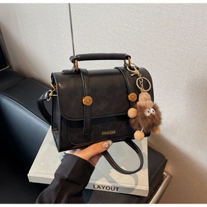 Close-up of vintage black leather handbag with gold buckles and a cute plush monster charm