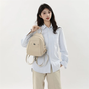 Detail of a beige oxford cloth backpack showing top handle grip and metal logo detail