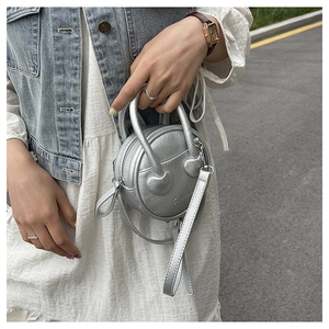 Detail of silver round mini bag with lychee texture and heart decoration being carried
