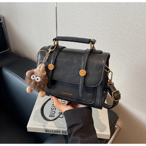 Detail of vintage black crossbody bag featuring bronze hardware and a plush monster charm