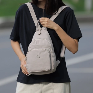 Detail of beige oxford fabric mini backpack with multiple zipper pockets on urban background