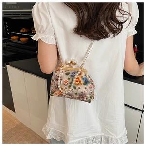 Detail of shell-shaped crossbody bag with bear embroidery and pearl strap worn by model