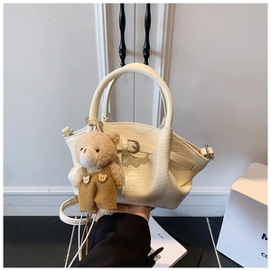 Detail of off-white crocodile texture handbag with cute brown plush bear charm
