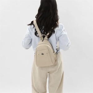 Detail view of cream Oxford cloth backpack showing adjustable leather straps on the back