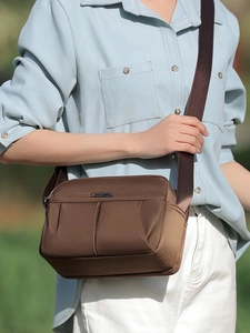 Brown nylon crossbody bag with metal logo and wide shoulder strap in outdoor natural light