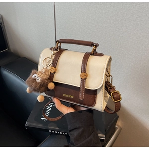 Detail of vintage bicolor crossbody bag with plush charm and golden metal hardware