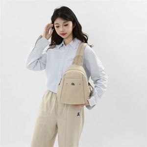 Detail of a beige oxford mini backpack showing metallic circular logo and nylon texture