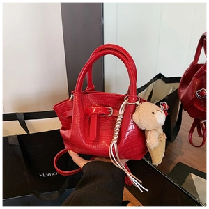 Detail of red crocodile texture handbag with metal buckle and plush bear pendant accessory