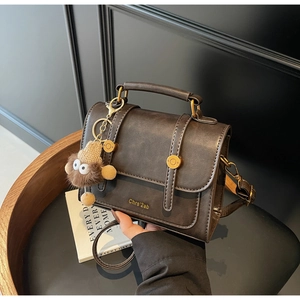 Detail of dark brown vintage handbag with gold hardware, plush charm, and top handle