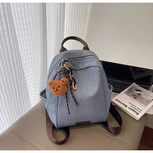 Detail of grey canvas backpack with brown straps and cute bear charm on leather seat