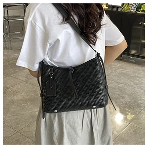 Detailed view of woven black crossbody bag with leather tag and silver base studs