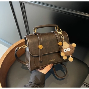 Detail of dark brown leather handbag featuring golden buttons and plush toy charm