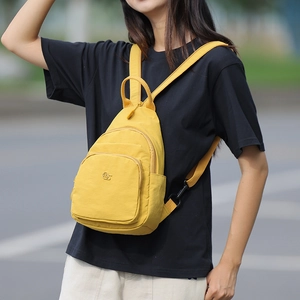 Detail of yellow nylon crossbody bag worn by model showing its multiple zipper pockets