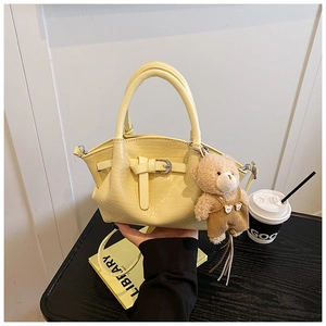 Detail of yellow crocodile pattern bucket bag with cute bear pendant on a wooden table