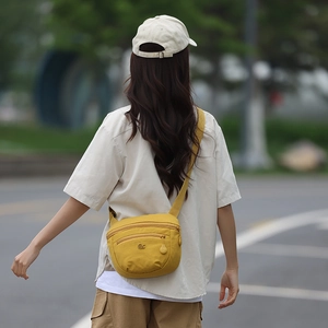 Outdoor shot showing back view of yellow canvas saddle bag with metal logo on crossbody strap