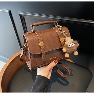 Detailed close-up of brown retro satchel with round metal buckle and plush monster charm