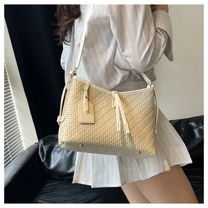 Detail of cream woven tote bag featuring decorative tassels and protective metal feet