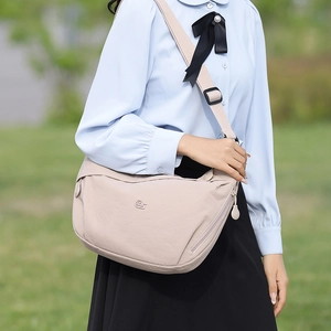 Close-up of beige moon-shaped canvas bag with adjustable strap in outdoor park setting