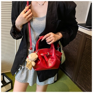 Detail view of red crocodile textured saddle bag with a cute teddy bear charm