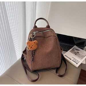 Detail of canvas backpack with leather handle and cute brown plush bear charm