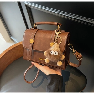 Detail of vintage brown leather bag with metallic buckles and a cute plush monster charm