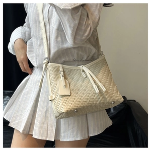Detail of cream woven shoulder bag with tassel zipper and adjustable strap on a model
