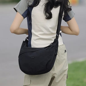 Detailed back view of a black nylon crescent crossbody bag with adjustable strap in nature