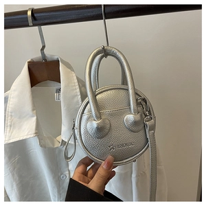 Detail view of silver round crossbody bag featuring heart decor and textured leather