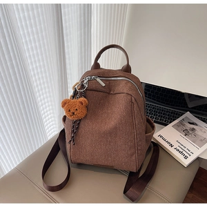 Close-up of brown textured canvas backpack featuring a plush bear charm and side pocket