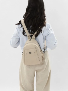 Minimalist beige oxford fabric backpack with metal logo shown on model from back view