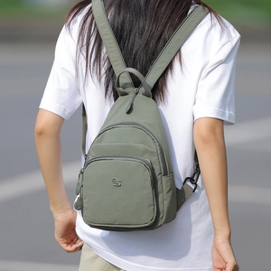 Outdoor shot of a dark green nylon crossbody backpack worn by a model in a white shirt