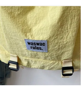 Detail of the logo patch and nylon fabric texture on a yellow minimalist backpack