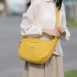 Detailed view of yellow canvas dumpling bag with metal logo and wide textile strap